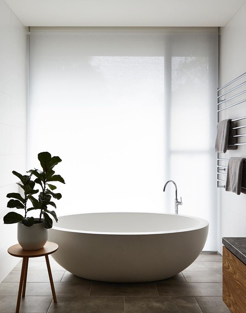 a statement freestanding bath against a large window with a large fiddle leaf fig plant on the left