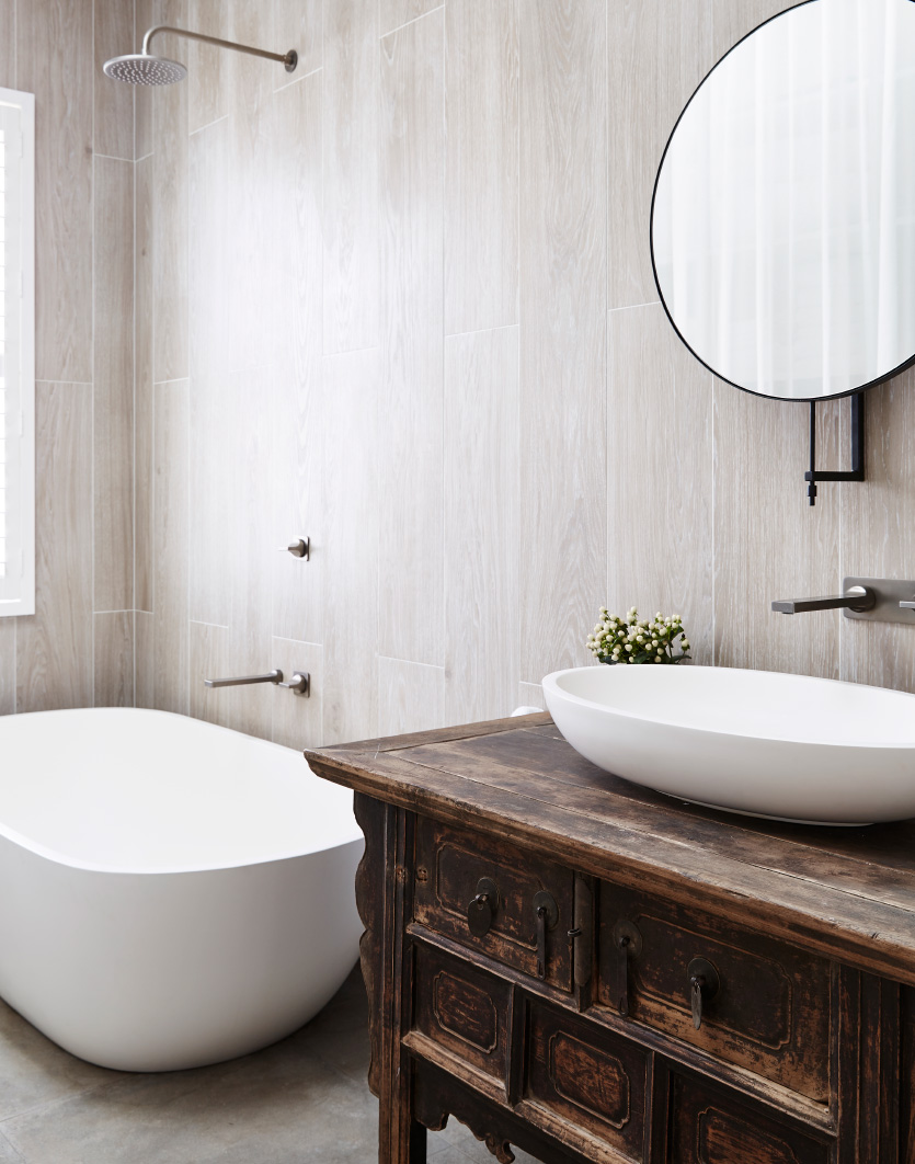 tiled bathroom featuring a stone freestanding bath and a countertop basin with a large round mirror