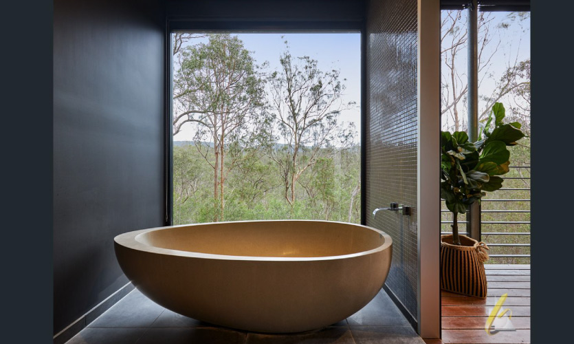 asymmetric bath placed near a large window with a view of a eucalyptus forest